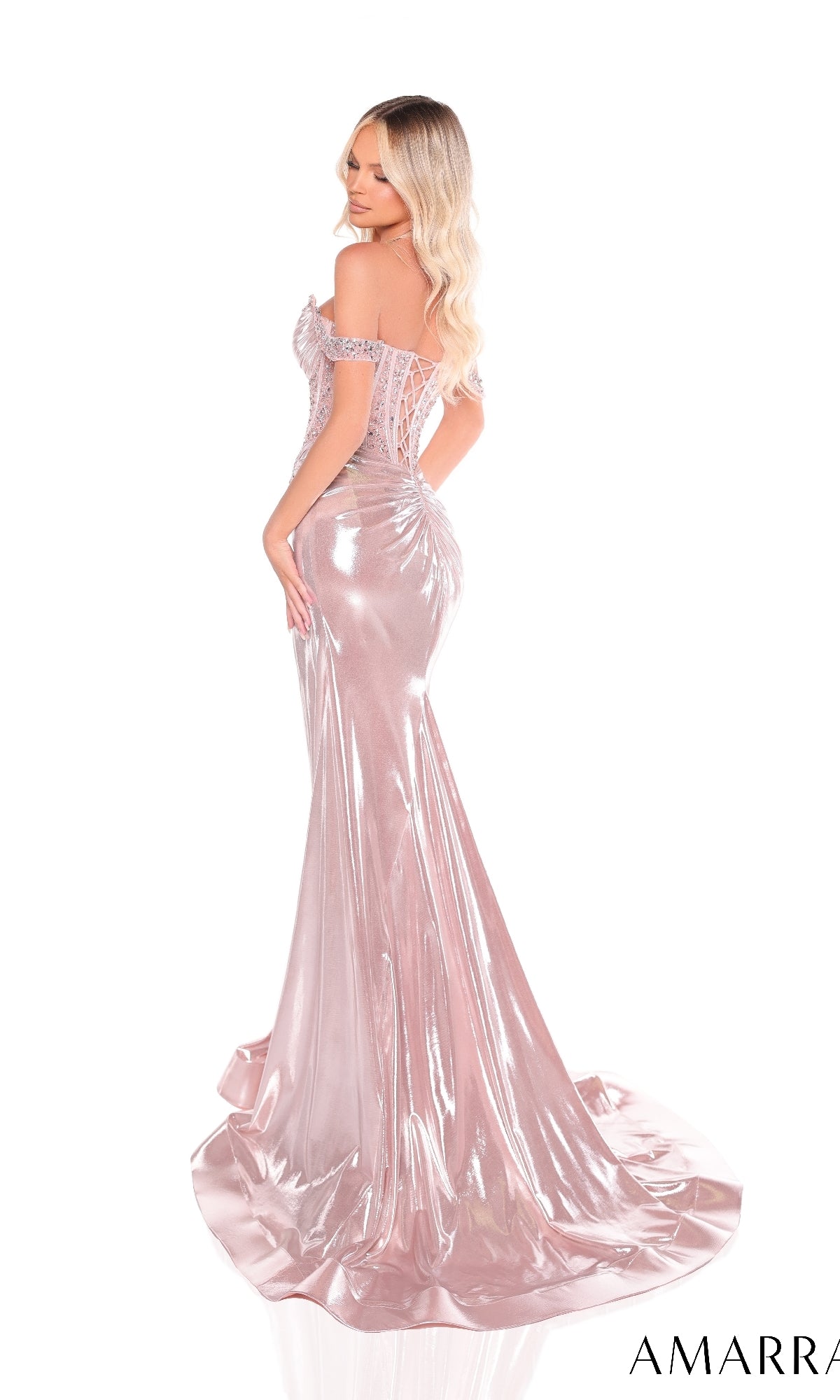 A woman poses with her back slightly turned, wearing the Amarra 88254 long prom dress—an off-the-shoulder, shimmering pink designer gown with a fitted silhouette and sweeping train.